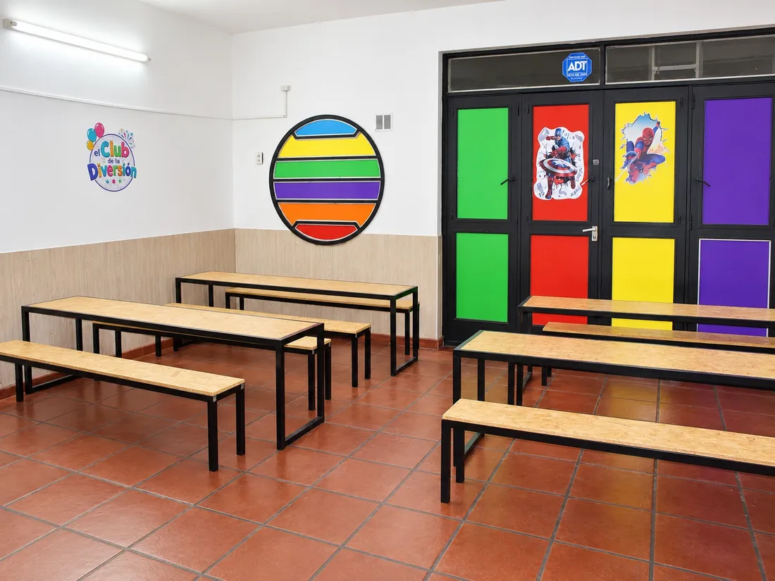 Mesas y bancos del comedor de los chicos frente a la puerta de colores